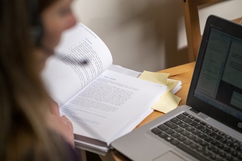 Image of woman with headset looking at a laptop with an open textbook