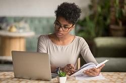 Image of a woman making notes in front of a laptop