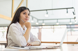 Image of a woman working at a laptop looking up thoughtfully 
