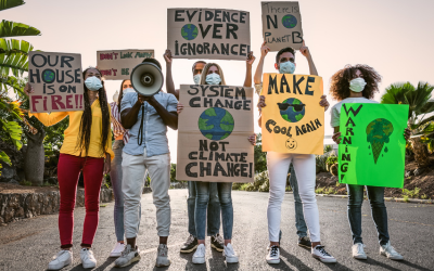 People involved in an environmental protest. They hold banners which include messages like 'Our house is on fire' 'System change not climate change' 'Evidence over ignorance' and 'There is no planet B'