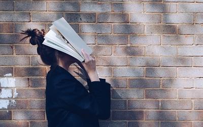 Photo of a stressed student with a book on her face